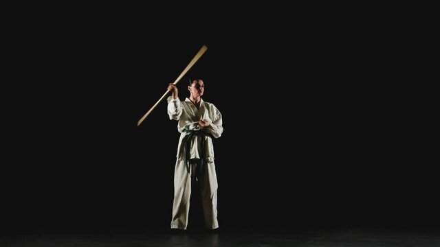 Young woman in kimono practicing with jodo on a black background