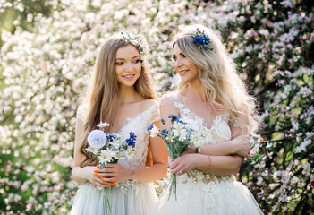 Natural beauty women in white dress with bouquet of flowers walks in the flowering garden, enjoying the blooming summer nature. Bridesmaids outdoor