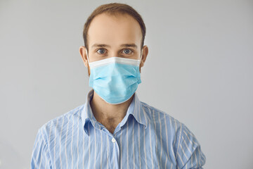 Portrait of happy handsome man in office shirt and blue medical face mask looking at camera. Profile picture of friendly company employee taking Covid 19 preventive measures in Coronavirus pandemic