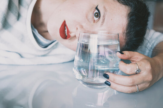 Portrait of a young woman hidden by a glass with a transparent drink