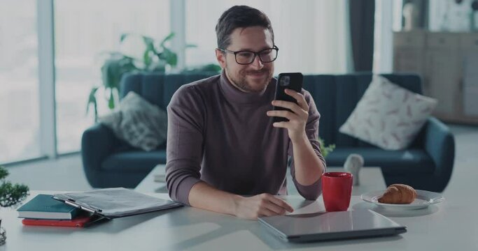Caucasian handsome businessman podcast creator working from home, using professiona equipment microphone and using smartphone typing messages busy in the apartment.