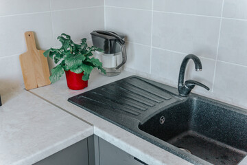 On the kitchen countertop are a chopping board, black containers, and a flower in a red board, next to the sink. The concept of minimalism and environmental friendliness in the kitchen