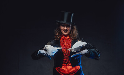 Fototapeta premium Serious female magician with white pigeons and top hat in dark background