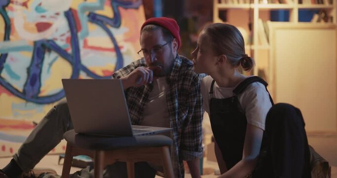 Couple of Professional Bearded Hipster Artist Coachi ng Teenger Girl Student Learning Oil Canvas Painting Skills in the Modern Studio. Artowork in background.