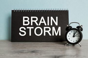A word BRAIN STORM on black notebook with clock. Concept for time management and business.