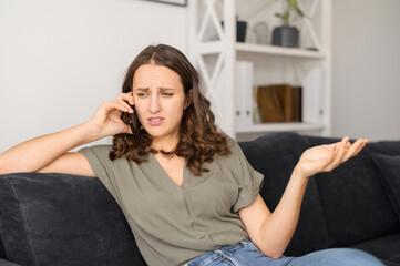 Fototapeta premium Annoyed woman talks over smartphone at home, irritated female has unpleasant phone conversation sitting on the couch