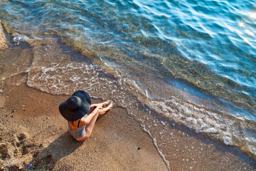 Top view of pretty woman in swimsuit posing on seashore. Beach, sea waves and foam. Summer vibes and summertime concept