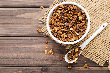 Tasty chocolate granola in bowl and spoon on brown wooden background