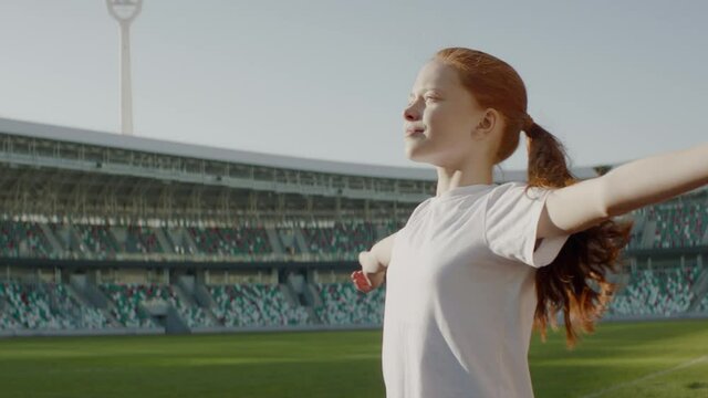 Portrait of Caucasian white girl walking onto the field of huge soccer football stadium, spreading hands, dreaming of becoming professional player, soccer star. Women sport concept