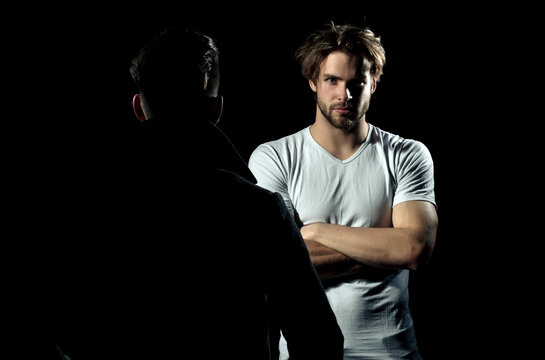 Two Men Standing Opposite. Focused Man, Serious Guy Having Conversation With Friend. Portrait Of A Serious Casual Men Standing With Arms Folded On Gray Background. Man In Shadow Dark.