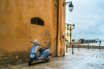 Un scooter bleu ciel dans une rue d'Ajaccio contraste avec les murs ocres jaune  des maisons dans les ruelles de la vieille ville corse.