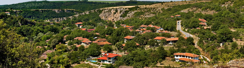 View of the beautiful village of Nisovo, Bulgaria, located below, above and in the high limestone cliffs, protected by magnificent deciduous trees 