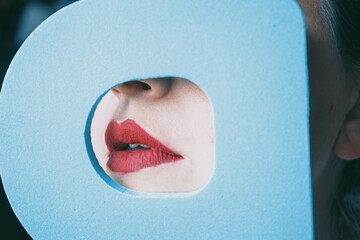 Young woman red lips behind a cover blue circle