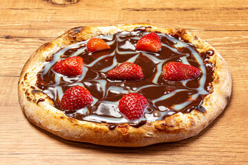 Chocolate pizza with strawberry and sour cream sauce served on a wooden table. Top view. Selective focus.