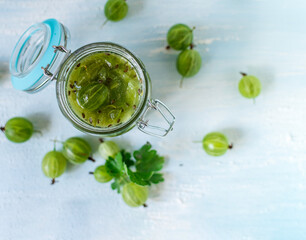 Gooseberry jam in a glass jar and berries scattered around. No-cook jam. Food background. Top view