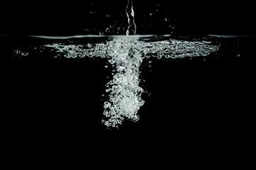 a jet of water on a black background. A splash and a bubble of air under the water.