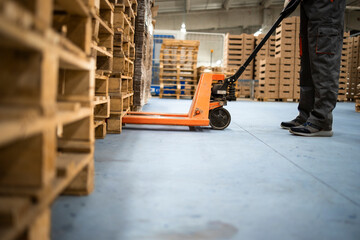 Working at warehouse. Low angle view of unrecognizable worker lifting palette with manual forklift. - obrazy, fototapety, plakaty