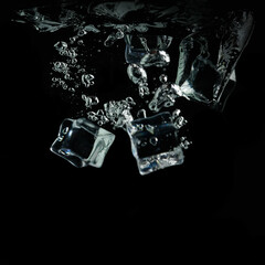 ice cubes fall into the water on a black background. Water splash and air bubbles under the water.