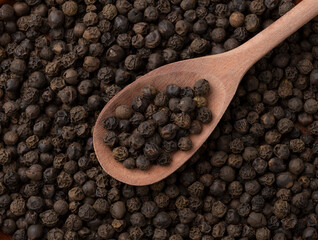 Top view, closeup of black pepper grains on a wooden spoon. Food backdrop