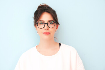 Closeup portrait of young beautiful  female in trendy summer white t-shirt.Sexy carefree woman posing near  blue wall in studio. Positive model having fun indoors. Cheerful and happy in spectacles