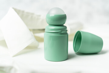 Green bottle of roll on antiperspirant deodorant lying on background of white blouse or shirt. Personal hygiene and body care concept.