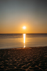 Obraz premium Dawn at sea. A yoga mat lies on the sand. Bright orange sky and water reflection. Vertical photo