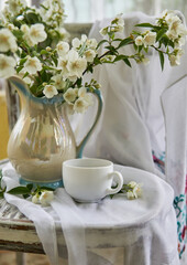 Jasmine flowers in a white vase. Stillife with jasmine and cup of coffee.