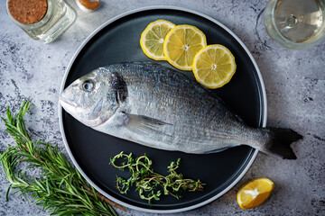 Raw fresh dorada fish with lemon slices and greens