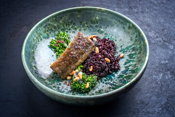 Modern style traditional fried skrei cod fish filet with baby broccoli, black rice and roasted pine...