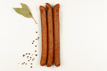 Three sausages are laid out on a white background, next to spices and bay leaf
