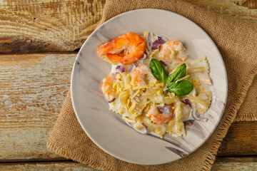 Farfalle pasta with shrimps in a creamy sauce on a gray plate on a wooden table on a linen napkin.