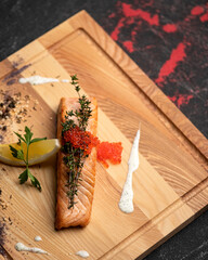 Piece of fried red fish garnished with red caviar and thyme on wooden cutting board. Salmon or trout baked with vegetables. Sea or river Fish cooked. Top view.