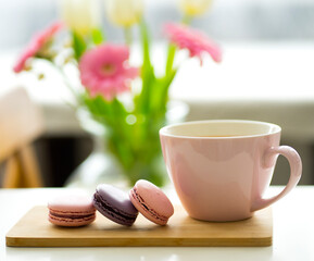 A pink cup with tea, multi-colored macaroon cakes, a bouquet of flowers. Delicate composition. Image with selective focus