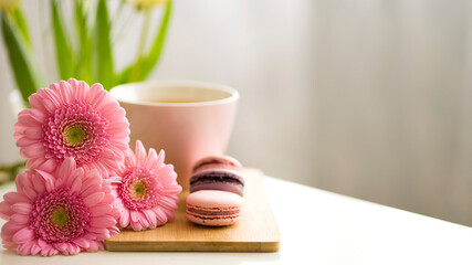 Beautiful composition of pink gerberas, macaroon cakes and a pink cup with tea