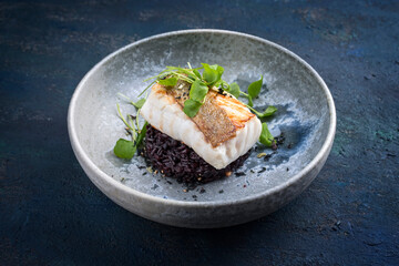 Modern style traditional fried skrei cod fish filet with portulaca lettuce, and black rice served...