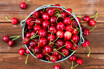 Freshly picked ripe cherries in a bucket on a wooden background, top view. Ripe red cherries in the metal bucket on a wooden background