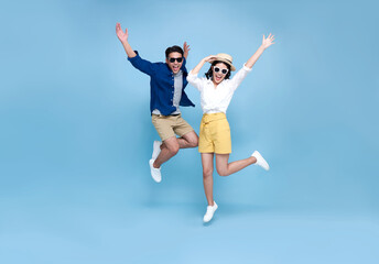 Happy Asian couple tourist jumping celebrating to travel on summer holiday isolated on blue background.