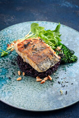 Modern style traditional pan-fried skrei cod fish filet in breadcrumbs with baby broccoli, black rice and portulaca lettuce served as close-up on ceramic design plate