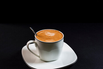 Coffee with milk in a decorative porcelain cup and with a spoon.Photography on a black background.