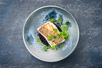 Modern style traditional fried skrei cod fish filet with portulaca lettuce, and black rice served...