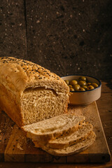 Homemade and artisan bread of morita chili and spices in a stick, a person with a knife cutting it into slices on a wooden table. Accompanied by olives, cheese and red wine.