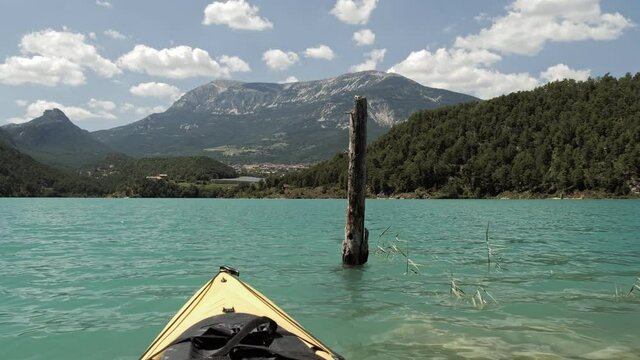 Kayaking on an emerald lake with beautiful mountain background. A yellow kayak sails past an old tree trunk sticking out of the water.