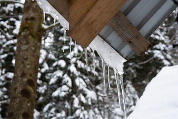Wooden structure in the winter forest. Icicles on the roof. They ate in the snow.