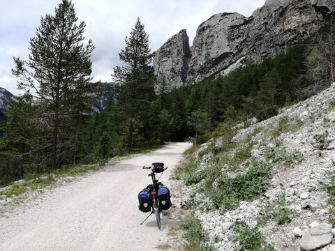 A touring bike on a gravel road in front of a mountain backdrop in the Alps.