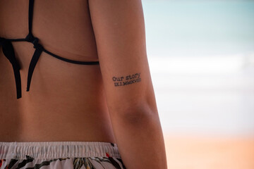 Tatuaje en el brazo de mujer morena en la playa