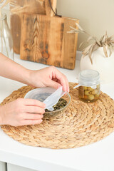 How to use as directed universal silicone lids for kitchen. Woman closes a glass cup with seeds and a jar of olives for long-term storage. Reusable eco-friendly kitchen products. Zero waste and