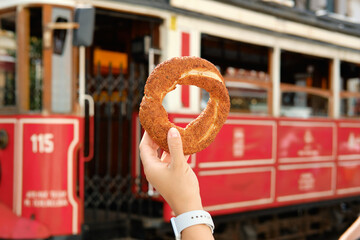 Girl holds a simit in her hand against the background of the famous red tram in Istanbul, Turkey. Traditional Istanbul simit.
