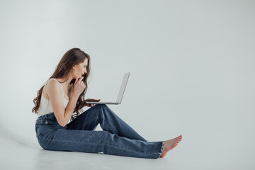 Portrait of woman in casual sitting on floor in lotus pose and holding laptop isolated over white...