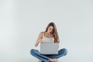 Portrait of a smiling casual girl holding laptop computer while sitting on a floor isolated over white background