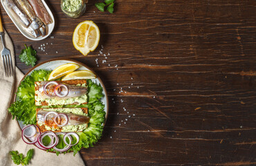 Two sandwiches on rye crusty bread with herring fillet, cream cheese and slices of red onion. Overhead on a dark rough wooden background with copy space